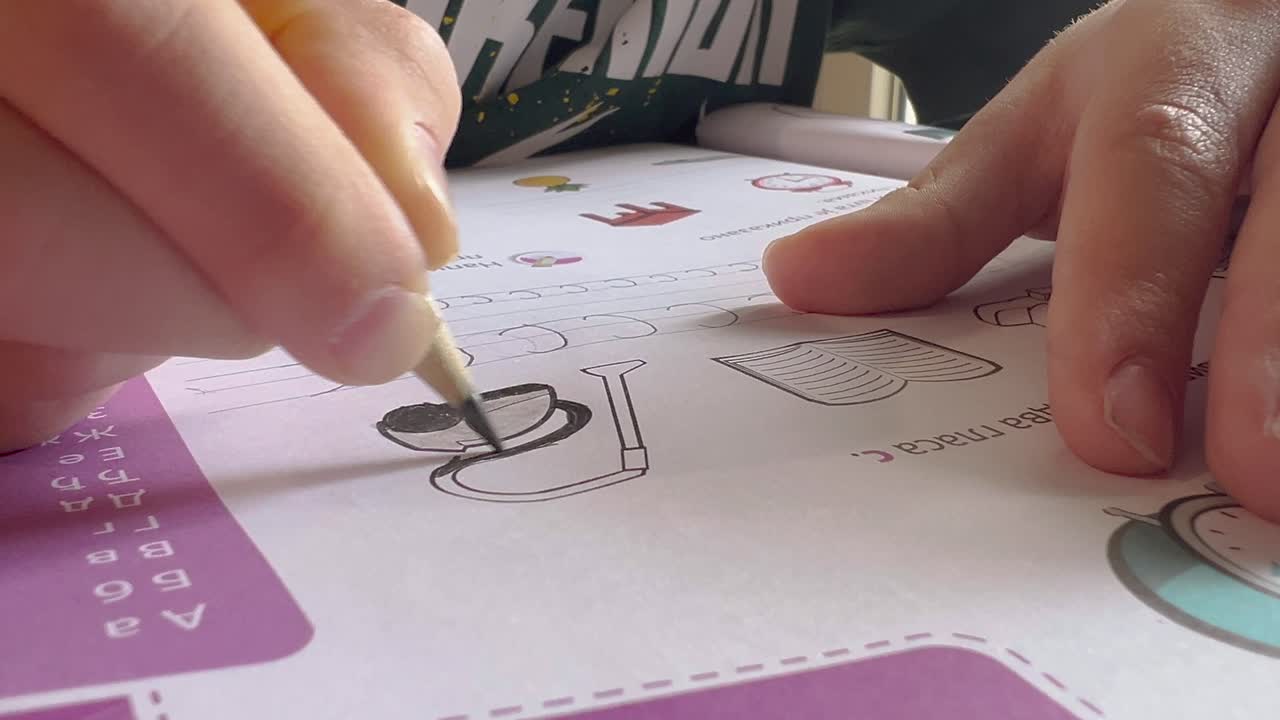 Schoolboy doing homework and coloring the drawing in the book