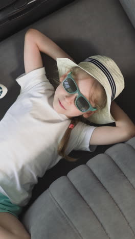 relaxed preschooler lies on sofa near airplane toy and suitcase in hotel room. little girl rests before activities on vacation upper close view