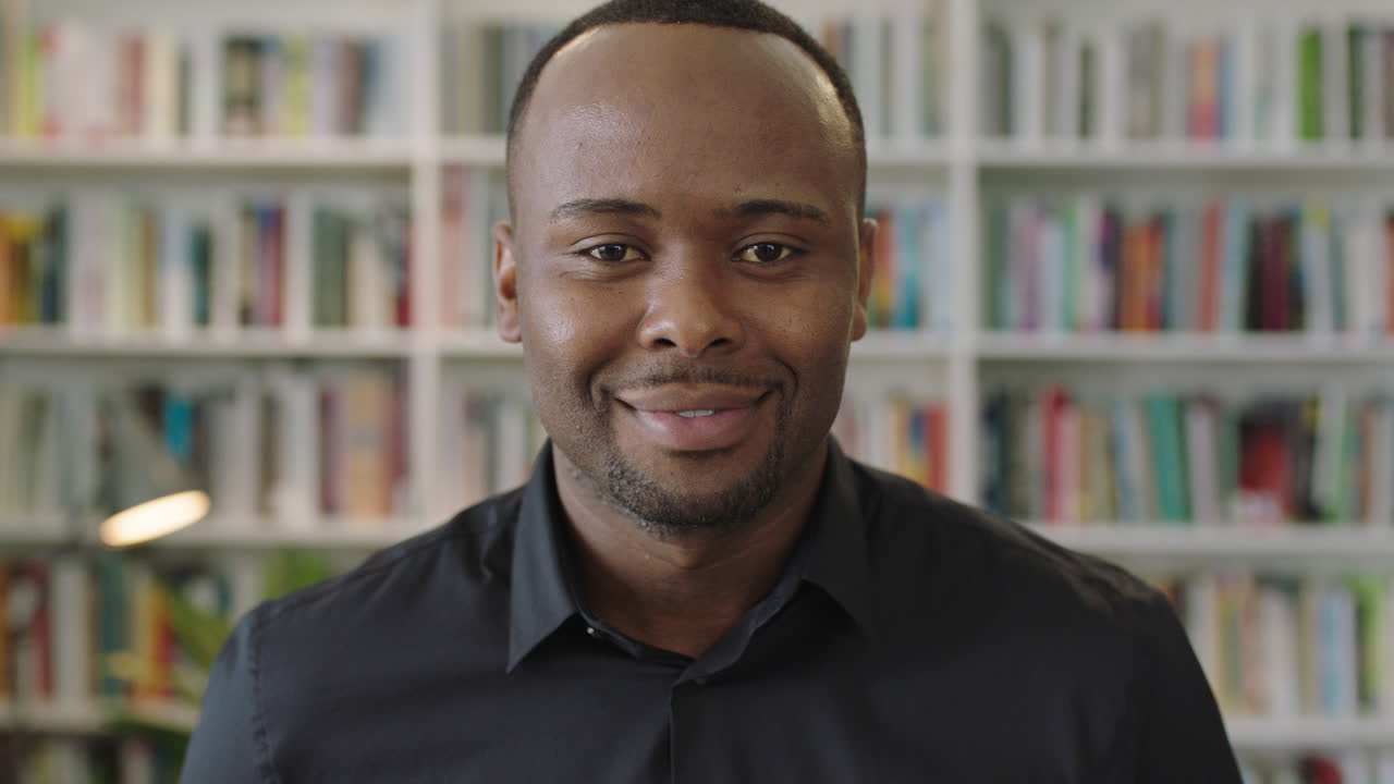 retrato de un joven afroamericano sonriendo mirando a la cámara de pie en la biblioteca