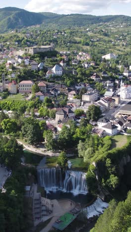 jajce with lush hills, traditional homes and its iconic central waterfall, aerial vertical view