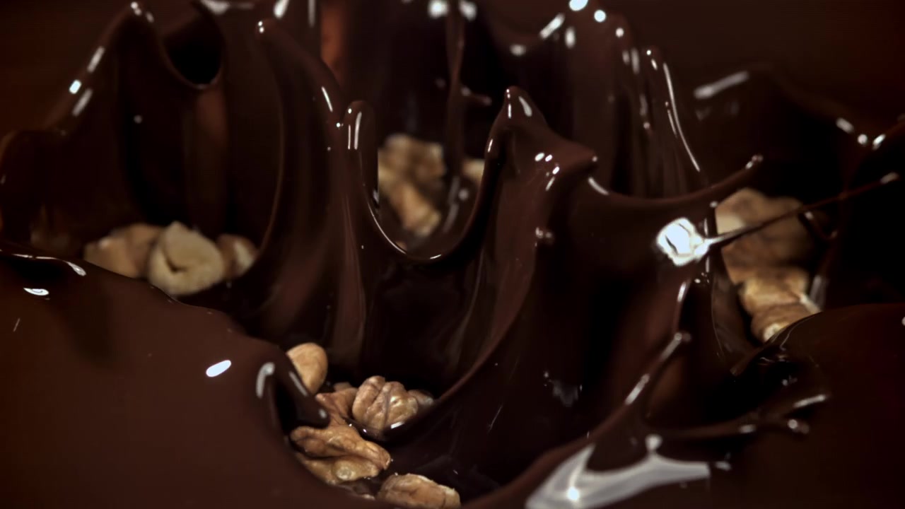 Noci che cadono e schizzano nel cioccolato fondente fuso al rallentatore