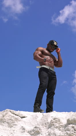 athlete man showing muscles on rocky mountain. handsome black african american man bodybuilder with naked torso posing on the rocky mountain peak. vertical video