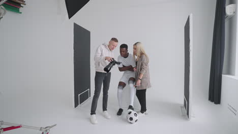 een fotograaf een voetballer een model en een regisseur kijken naar foto's van een fotoshoot voor de cover van een reclametijdschrift op een camera