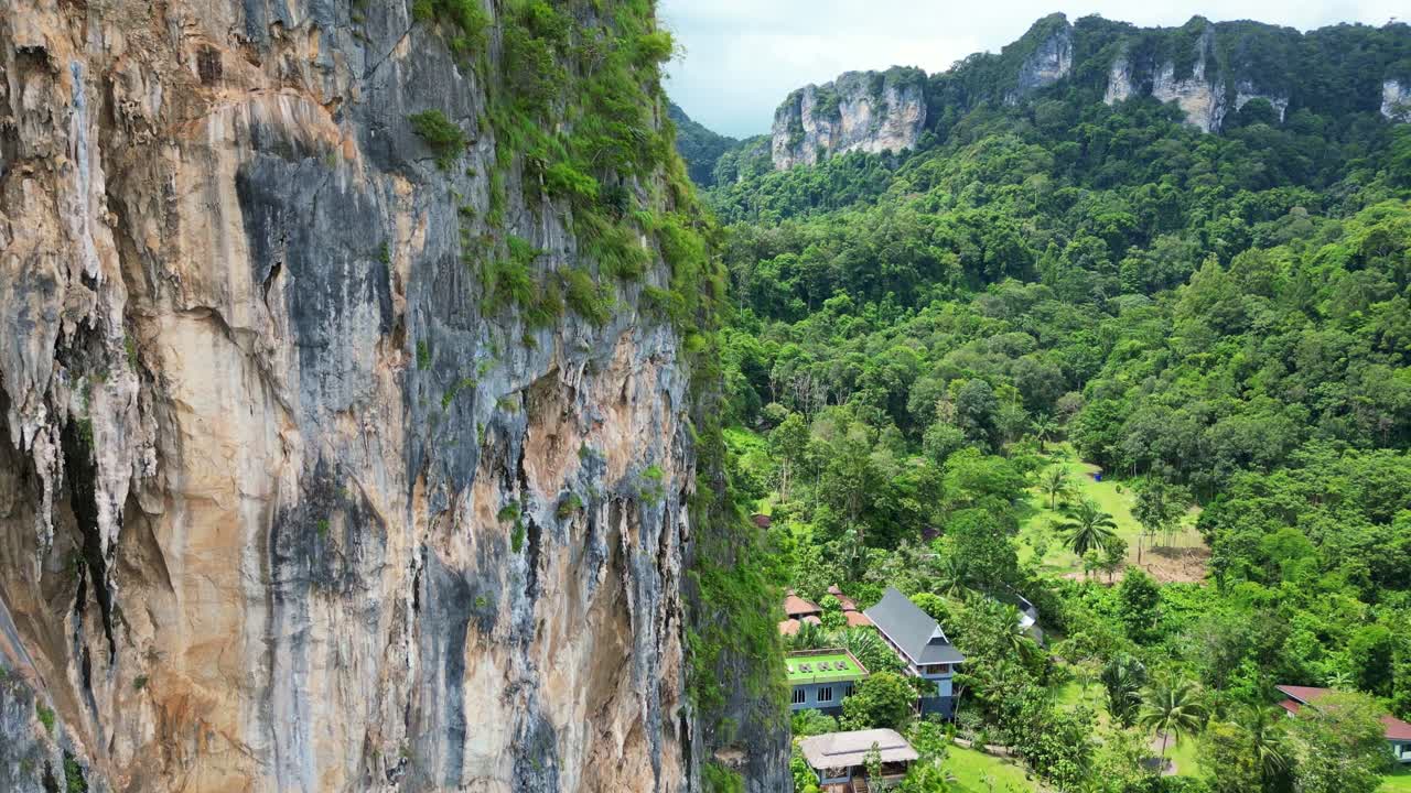 A scenic view of a rocky cliff surrounded by lush green forests and a tropical landscape with residential buildings.
