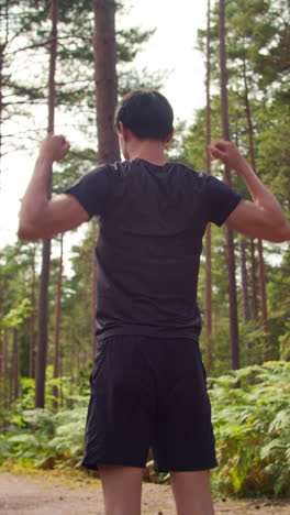 video de vista trasera vertical de un hombre calentándose y estirando los brazos antes de hacer ejercicio corriendo por el bosque