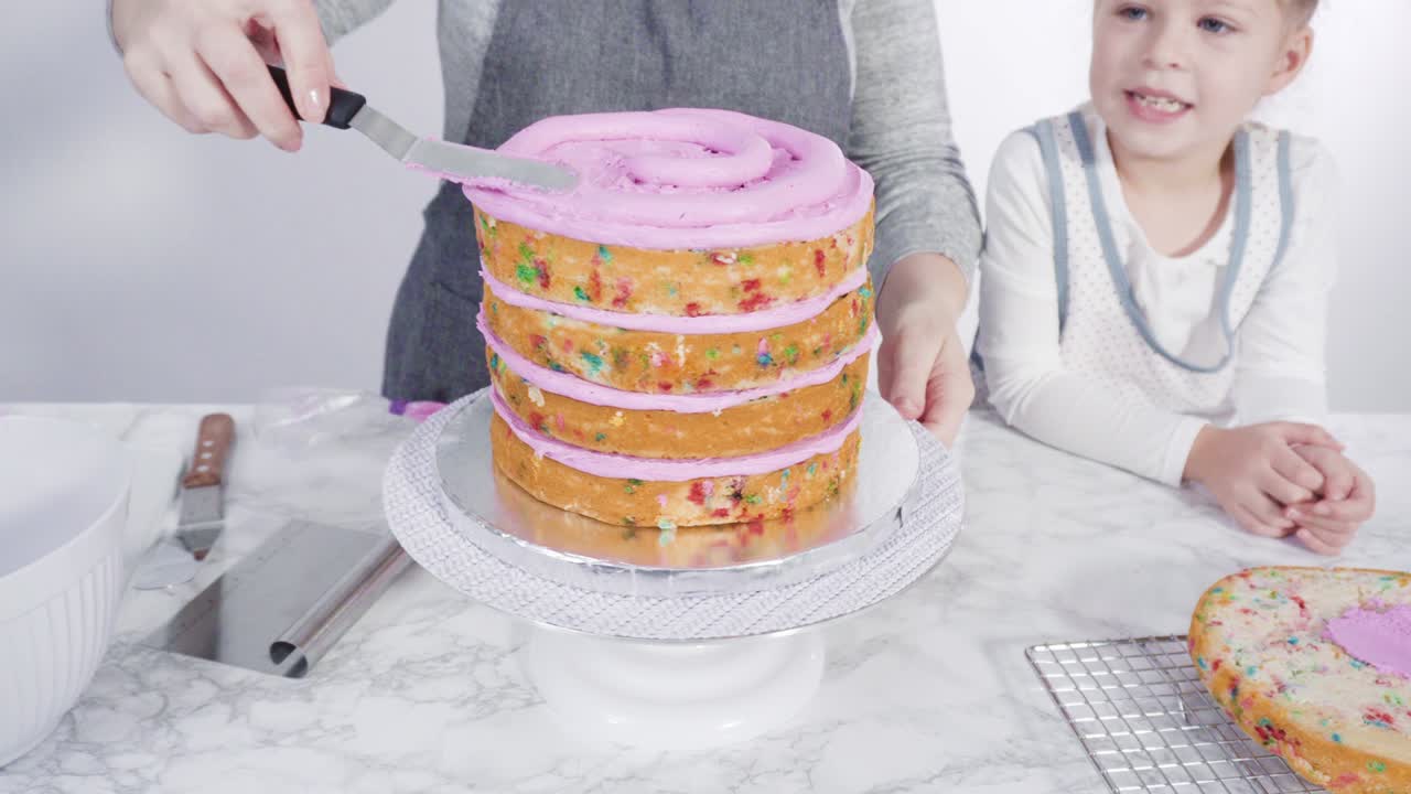 분홍색 버터크림 글래싱으로 둥근 페티 케이크 층을 글래싱합니다.