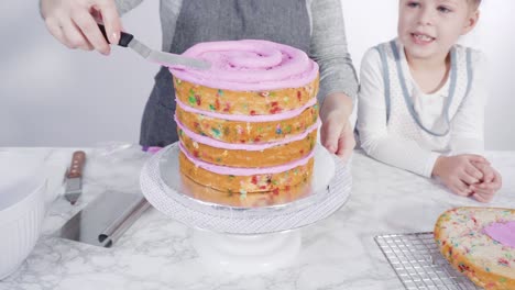 el glaseado de las capas redondas del pastel funfetti con glaseado rosado de crema de mantequilla.