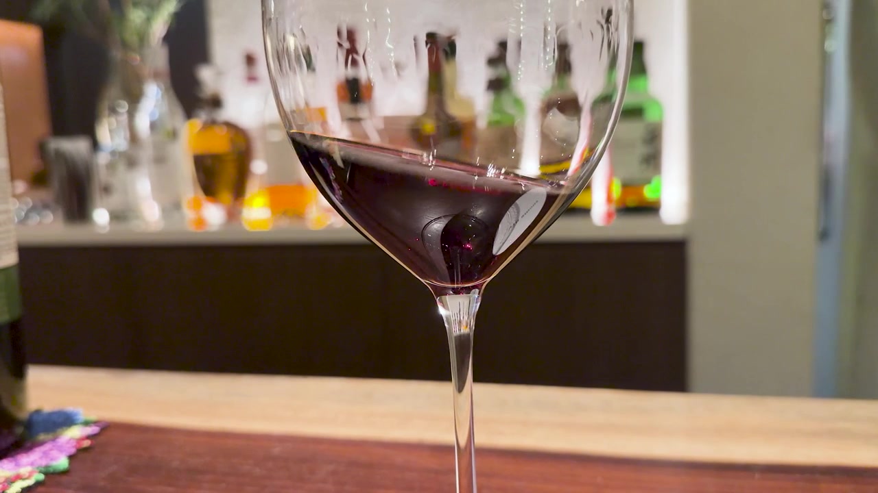 Primo piano di vino rosso che vortica in un bicchiere su un bancone da bar in legno.