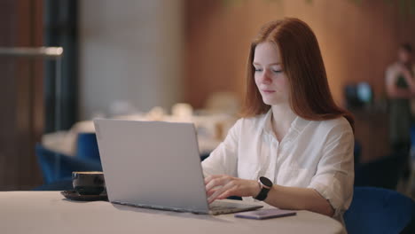 young red-haired female professional writing an important email from her home. modern living room. remote working. serious woman search for inspiration make decision feel lack of ideas