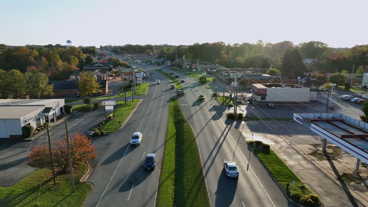 Aerial flyover american highway with driving cars at sunset time. Colorful trees in autumn season. Construction site of gas station in suburb. Wide shot.
