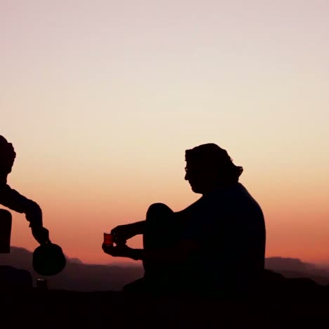 a bedouin man pours tea and toasts a western tourist in a silhouette shot