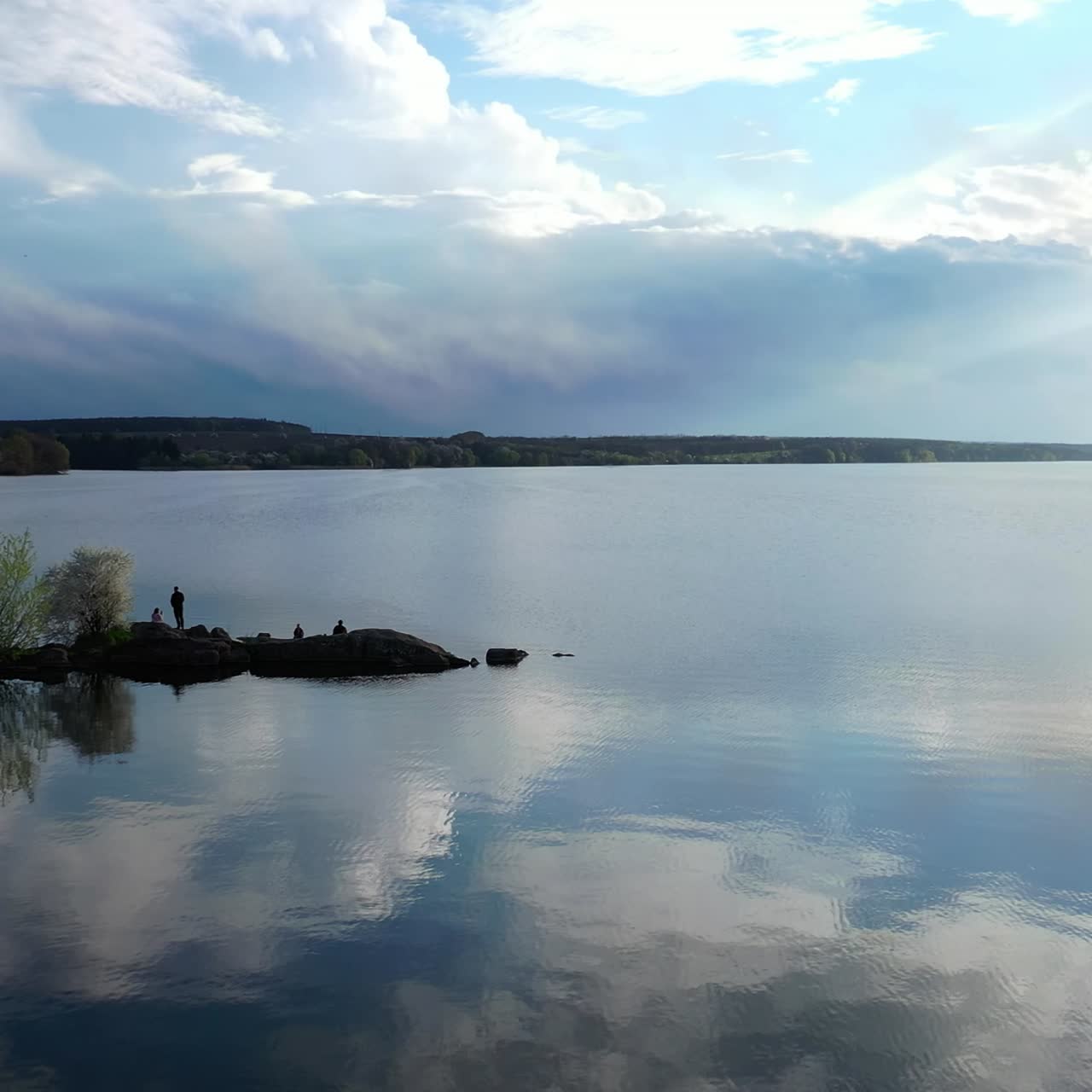 Beautiful river on nature landscape in spring. People rest near the water on stones in springtime. Blooming trees on a bank of the river