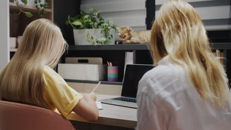 woman helping a girl who is working with a laptop in the classroom