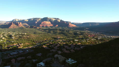 Toma-De-Drones-De-Sedona,-Arizona,-EE.UU.,-Edificios-De-La-Ciudad-En-Un-Valle-Verde-Bajo-Colinas-De-Roca-Roja-Al-Amanecer.