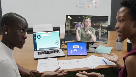 mujeres de negocios diversas en la oficina usando computadoras con videollamadas y mensajería artificial en pantallas