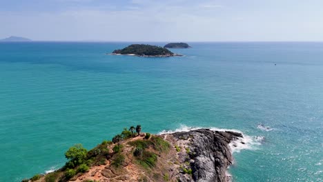 drone footage captures the stunning coastline of promthep cape, phuket, showcasing vibrant turquoise waters and rugged cliffs under clear skies