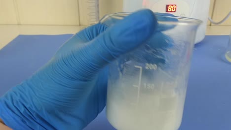 macro shot of a cosmetic emulsion being prepared in a laboratory. the video captures the operator's gloved hands mixing ingredients in a beaker,