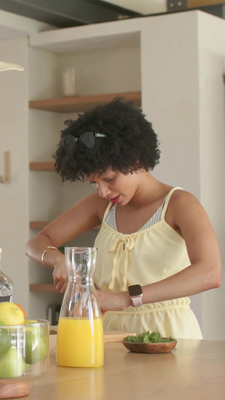 Video verticale: Donna in maglietta gialla che affetta agrumi in cucina, prende il telefono e prepara uno spuntino.