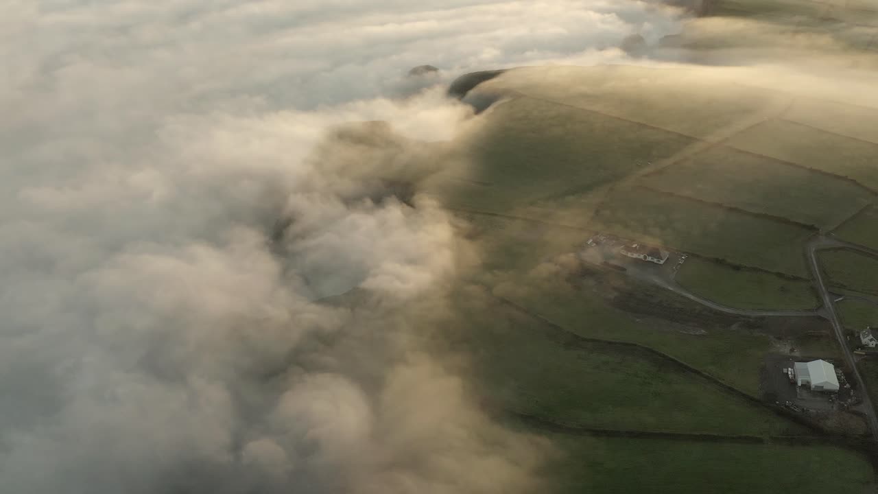 Thick fog rolls over Irish coastal farm land in sunrise cloud aerial