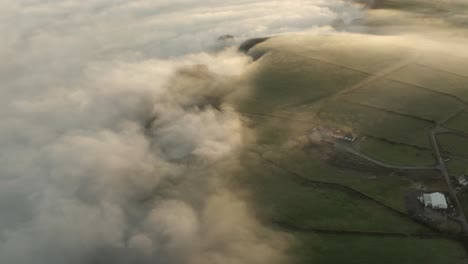 thick fog rolls over irish coastal farm land in sunrise cloud aerial