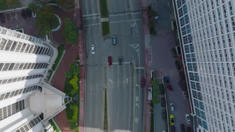 Birds-eye-view-of-cars-driving-on-wide-road-in-city-in-tropical-area.-Modern-high-rise-apartment-buildings-and-palm-trees-along-road.-Miami,-USA