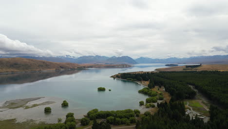 aerial tracking shot over the calm shore of lake tekapo new zealand on an overcast cloudy day