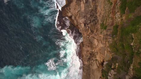 Ocean-waves-crashing-and-hitting-against-cliff-and-rocks-bird-eye-view-aerial-drone-shot