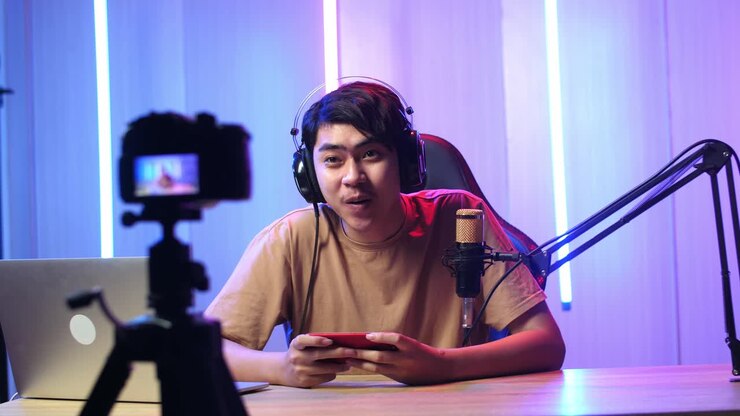 Uomo asiatico che tiene in mano un telefono cellulare e parla alla telecamera durante una diretta streaming.
