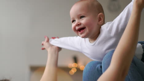 A-baby-in-a-white-t-shirt-lies-on-his-mother's-lap-imitating-the-flight-of-an-airplane