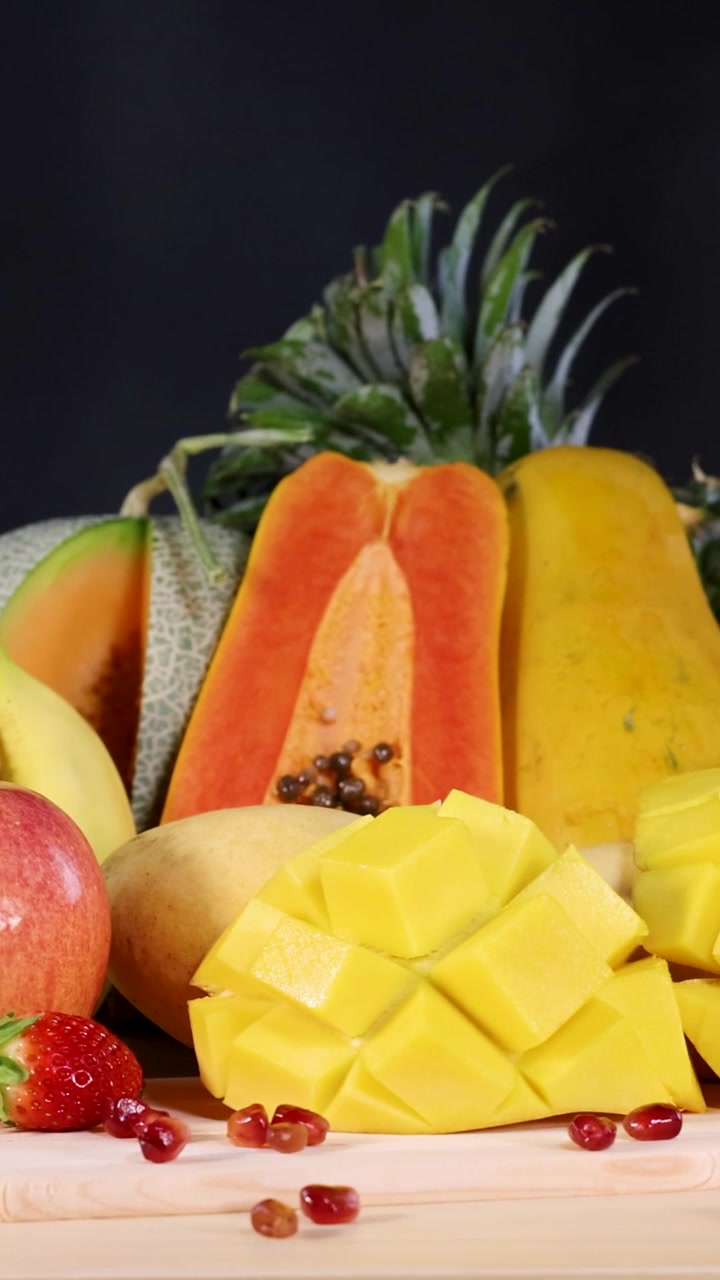Una vivace esposizione verticale di mango, papaia, fragole e mela a fette su una superficie di legno.