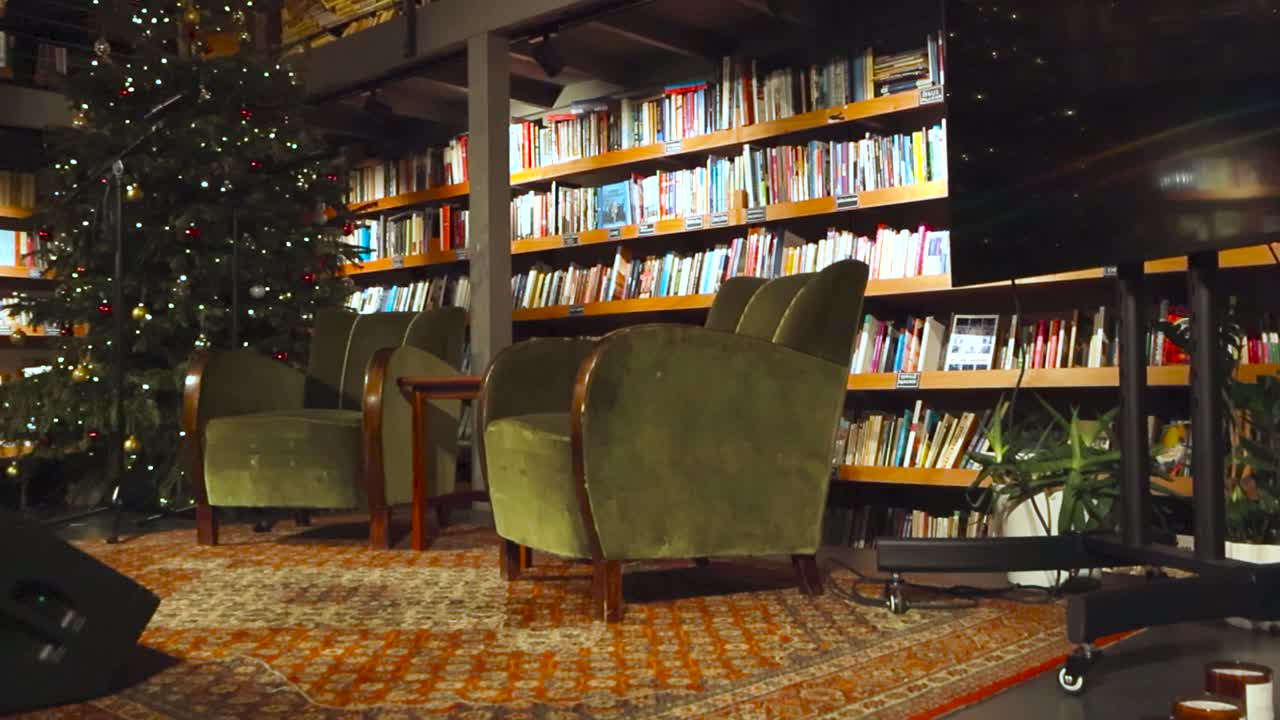 Stage for reading or podcasts in a vintage and retro library with two couches on the stage with studio monitors and retro carpet. Bookshelves with books are in the background with Christmas tree also.