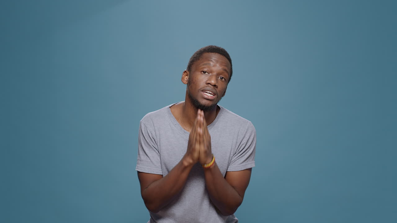 Hopeful man doign prayer gesture with hands in front of camera