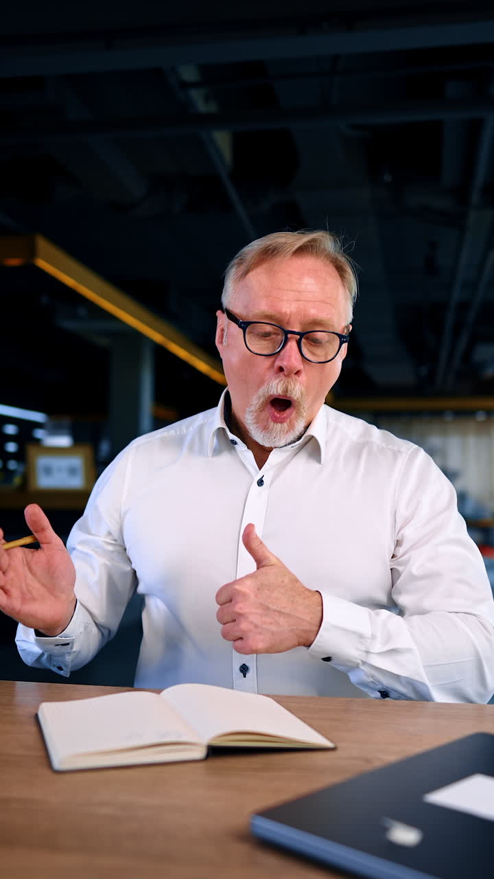 Bearded man in white shirt having lots of work to do. Man looks at his daybook and gestures that everything is ok. Vertical video.