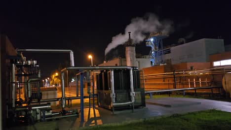 general shot at night in a chemical factory with time laps of starry sky and steam chimney releasing steam
