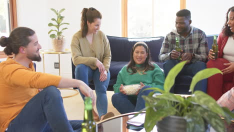 happy diverse male and female friends relaxing at home together drinking beers and eating popcorn