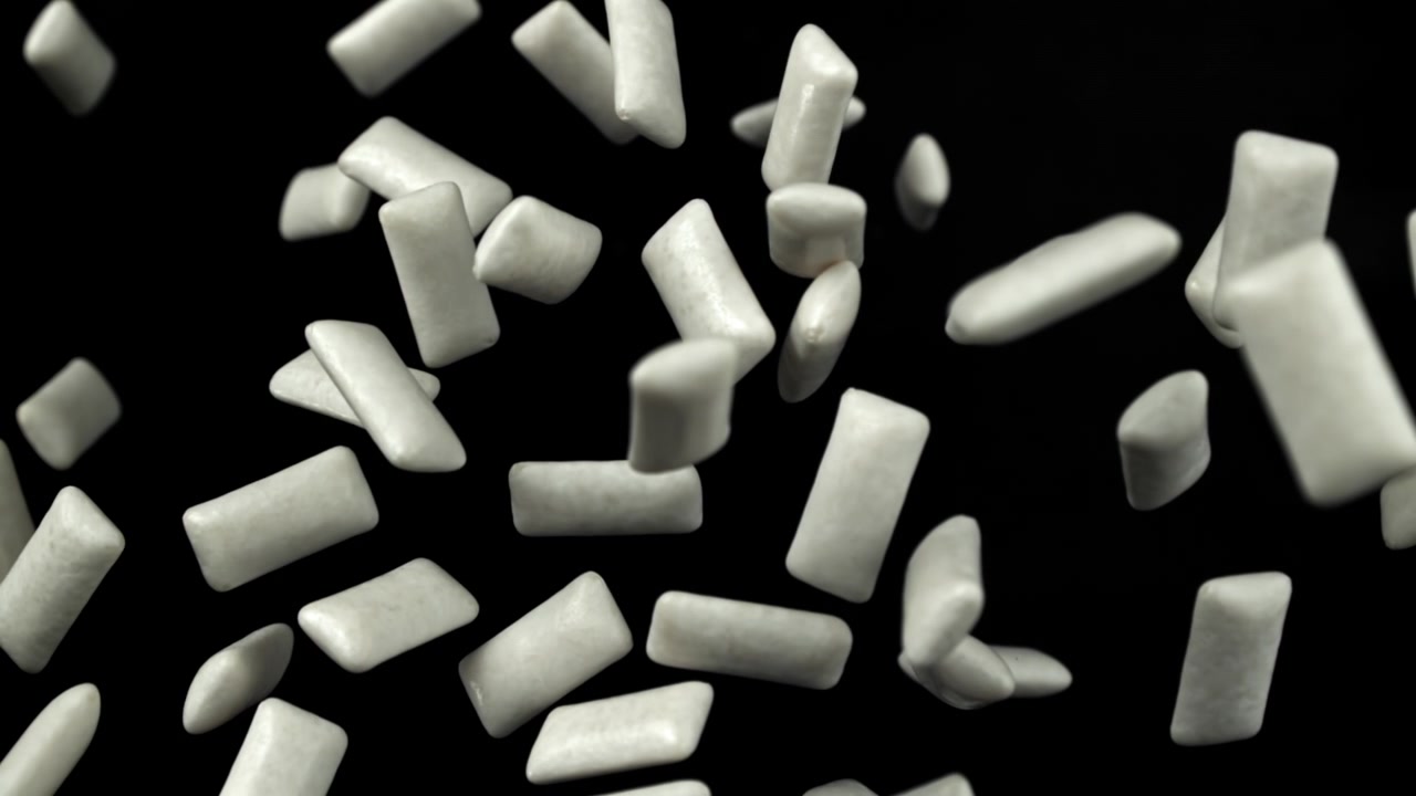 Pezzi di gomma da masticare bianca che cadono al rallentatore su sfondo nero.