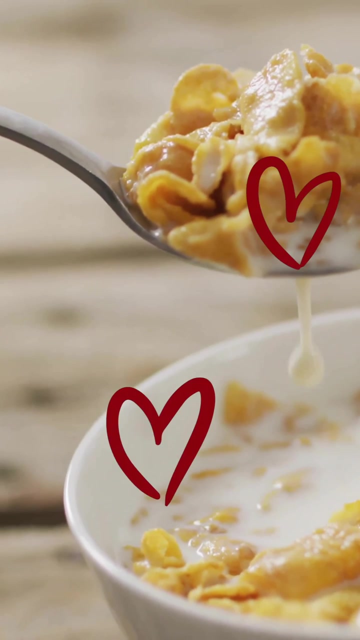 Cucchiaio che solleva cornflakes con latte, animazione di forme a cuore su una scena di colazione