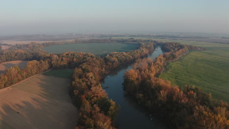 Toma-Aérea-De-Gran-Angular-Del-Pequeño-Río-Danubio-Con-Dos-Pájaros-Blancos-Volando-Y-Coloridos-Bosques-Otoñales,-Campos