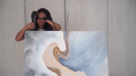 Artista-Femenina-Secando-La-Parte-Superior-De-Un-Lienzo-De-Pintura-Con-Un-Secador-De-Pelo-En-El-Estudio