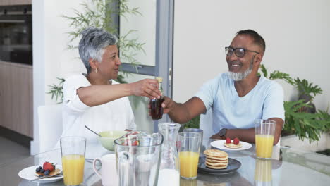 biracial couple enjoys a hearty breakfast, the man opening a bottle of champagne