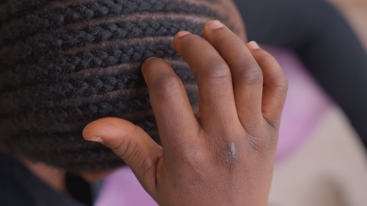 overhead black teen adjusting neat cornrows, purple shirt visible, fingers smoothing pattern, personal grooming ritual, upbeat morning, protective styling, textured hair and scalp detail, confident
