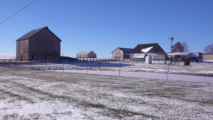 Inquadratura d'apertura di una classica e bellissima fattoria con casa colonica e fienili in una piccola città nel Midwest rurale americano, sotto la neve invernale