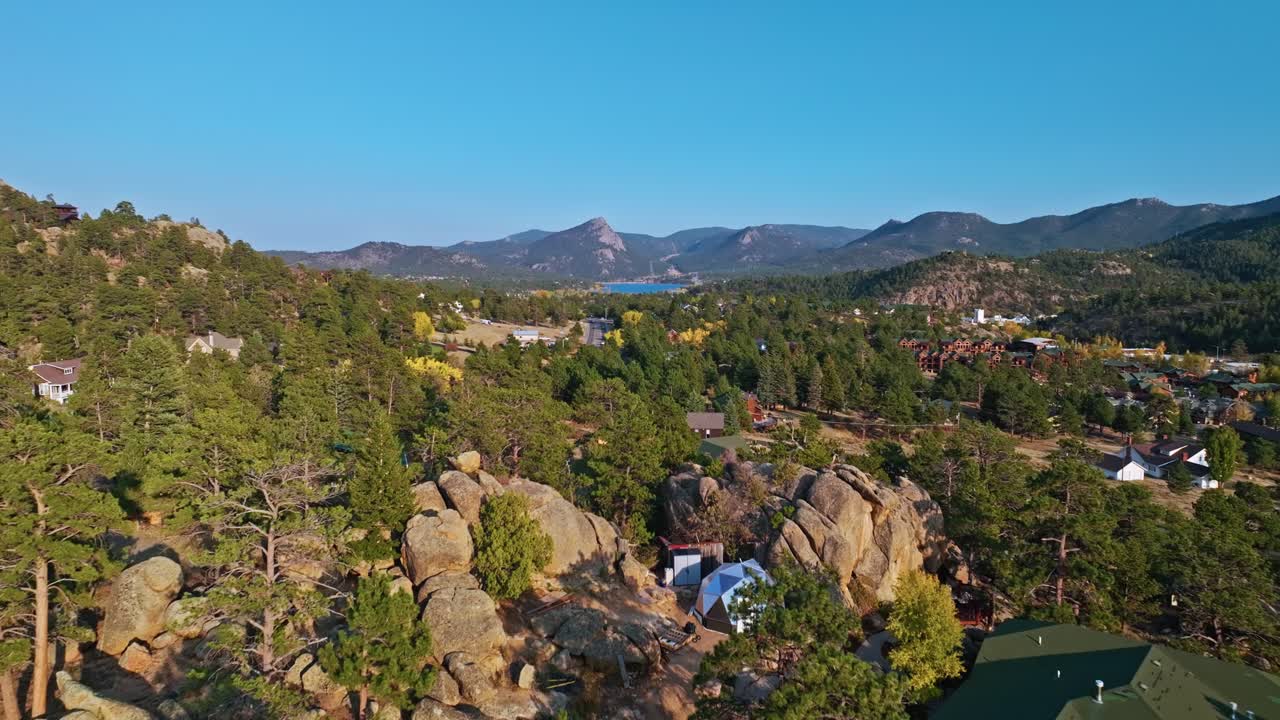 Aerial drone dolly of Estes Park in fall, sunflare over mountains and bright autumn foliage