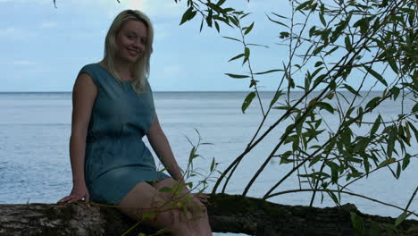 Young-woman-sitting-on-a-large-tree-branch-suspended-by-the-water