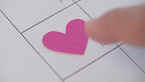 index finger push pink heart inside the box of valentine's day date on calendar