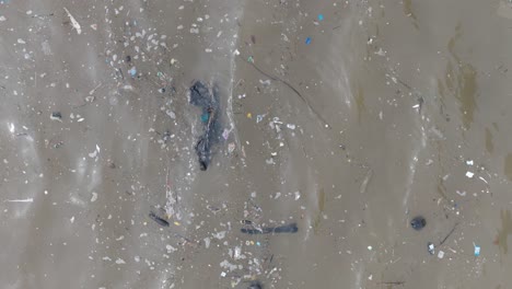 Cámara-Lenta,-Baja-Altitud,-Arriba-Hacia-Abajo,-Disparo-De-Drones-De-Un-Océano-Contaminado-Lleno-De-Basura-Y-Escombros-Flotantes-Y-Escurrimientos-De-Aguas-Residuales-Fangosas-En-Bali,-Indonesia