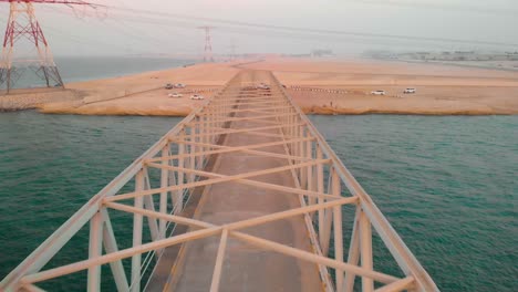 Drone-Vuela-Sobre-Un-Increíble-Puente-De-Hierro-Oxidado-Abandonado-Con-Torres-Eléctricas-Rojas-Y-Blancas-En-La-Escena-Del-Fin-Del-Mundo,-Antena