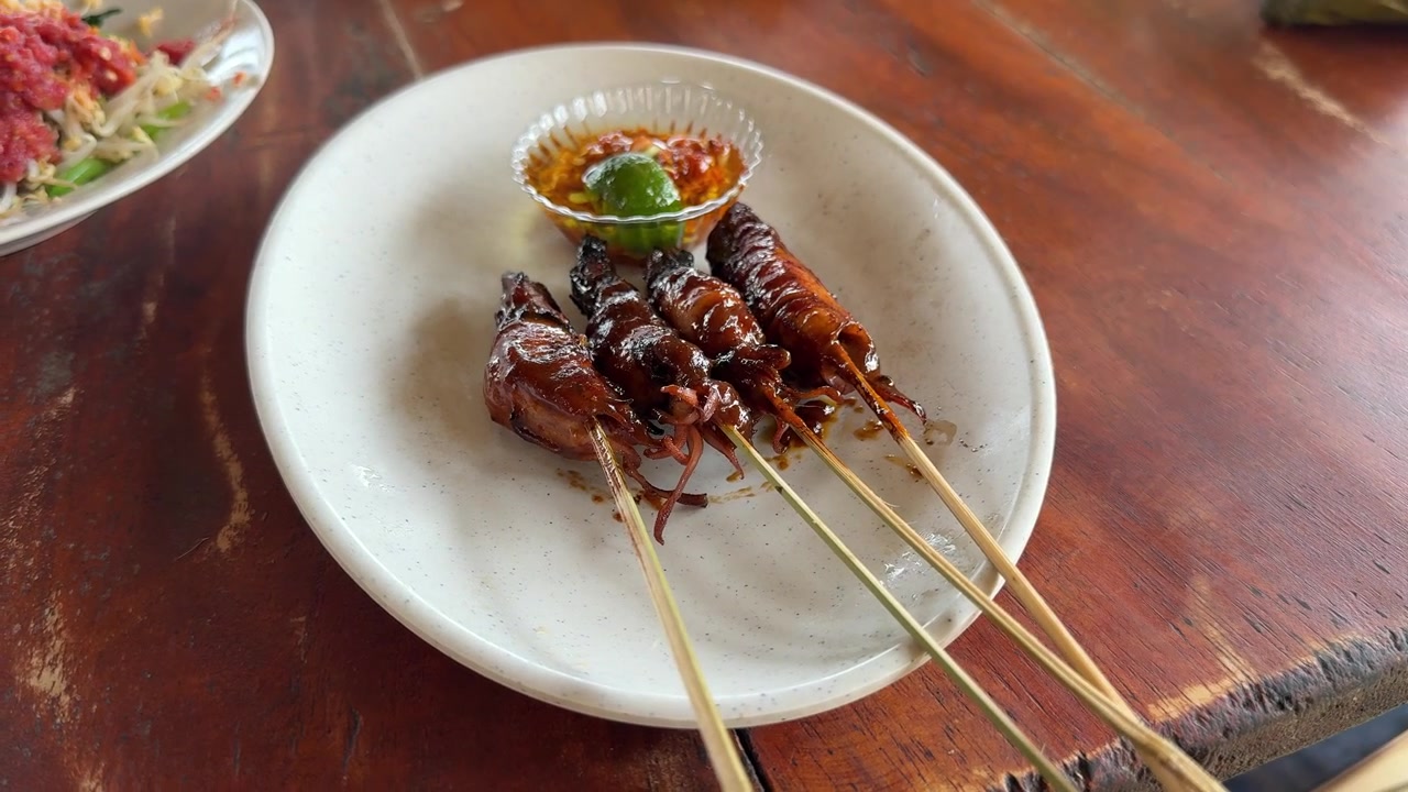 Herkullisia grillattuja mustekalavartaita (Sate Cumi) chilinkastikkeen kera puupöydällä.