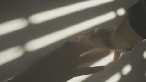 man's hand touches wall with hard window shadow projected on it