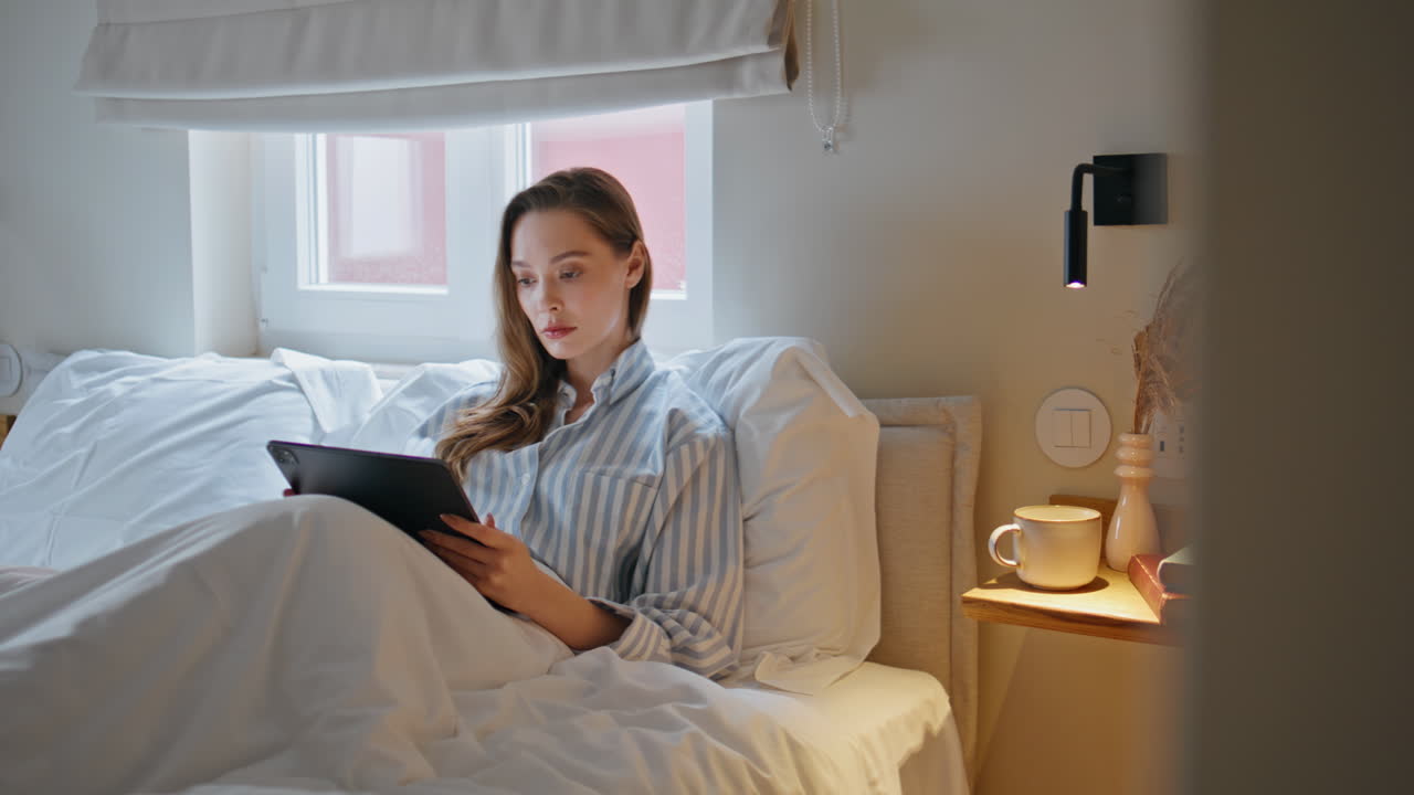 Girl using tablet bed reflecting modern leisure activity. Serious woman student